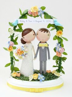 a wedding cake topper with a bride and groom in front of a floral arch