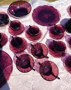 a table topped with lots of purple glass plates and bowls on top of a white cloth