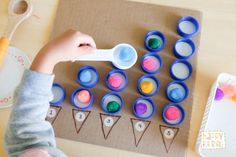 a child is holding a spoon in front of some cupcakes on a table