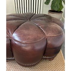 a brown leather ottoman sitting on top of a rug next to a potted plant