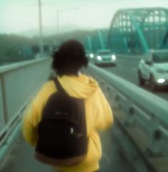 a person with a backpack walking on a bridge over water and cars in the background