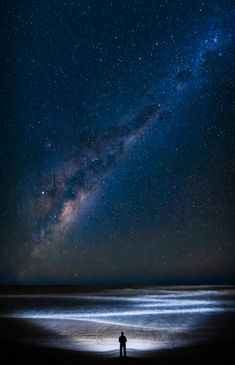 two people are standing on the beach looking at the stars