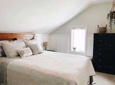 a bed sitting under a window in a bedroom next to a dresser and lamp on top of a hard wood floor