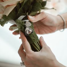 a person holding a bouquet of flowers with a dog brooch attached to the flower