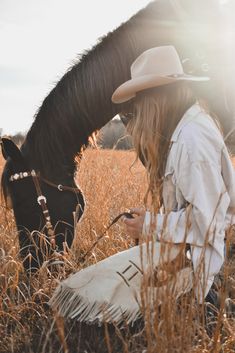 a woman sitting on the ground next to a horse in a field with tall grass