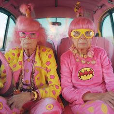 two older women in pink and yellow outfits sitting on the back of a car together