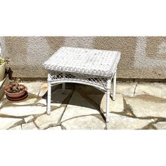 a white wicker table sitting on top of a stone floor next to a potted plant