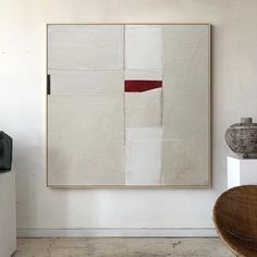 a painting hanging on the wall next to a wicker chair and vase in a white room