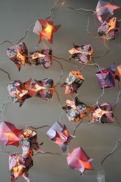 several origami pieces are hanging on a chain with lights in the shape of stars