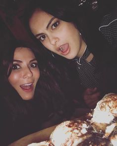 two beautiful women standing next to each other in front of a table filled with pastries