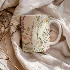 a coffee cup sitting on top of a bed next to dried flowers