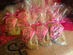 some cookies in the shape of cowboy boots are wrapped in plastic and tied with pink ribbon