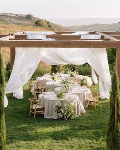 an outdoor table set up with white linens and greenery