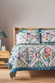 a bed with a blue and white quilted comforter on top of it next to a night stand