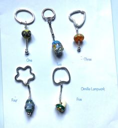 six keychains with different designs on them sitting on top of a piece of paper