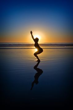 a person standing in the water at sunset with their arms up and legs spread out