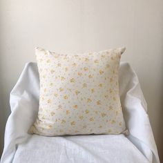 a white pillow sitting on top of a bed next to a white wall with yellow flowers