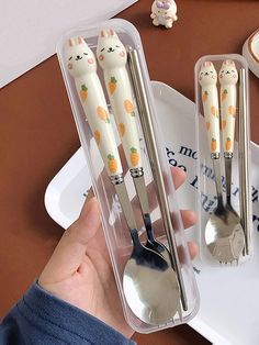 a person holding two spoons with cats on them in a plastic container next to other utensils