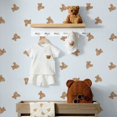 a teddy bear sitting on top of a wooden shelf next to a baby's clothing rack