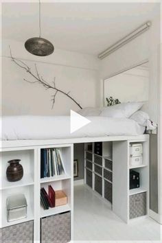 a white bed sitting under a mirror next to a shelf filled with lots of books