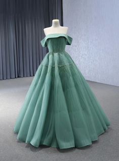 a green dress is on display in front of a gray wall and curtained window