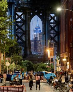 people are walking on the sidewalk in front of a bridge and some buildings at night