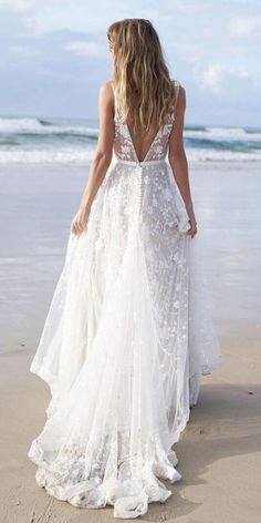 a woman standing on top of a beach next to the ocean wearing a white dress