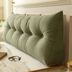 a green pillow sitting on top of a bed next to a pair of eyeglasses