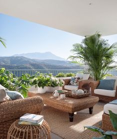 a living room with wicker furniture and plants on the balcony overlooking the mountain range