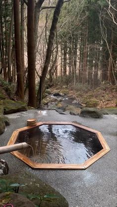 an outdoor hot tub in the middle of a forest with rocks and trees around it