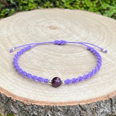 a purple string bracelet with an amethorate bead on it sitting on top of a tree stump