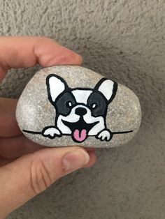 a hand holding a small rock with a dog on it's face and tongue sticking out