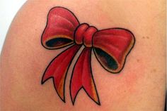 a red bow tattoo on the back of a woman's shoulder