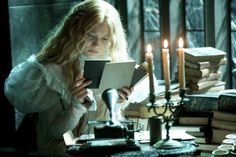 a woman sitting at a table with books and candles in front of her, reading a book