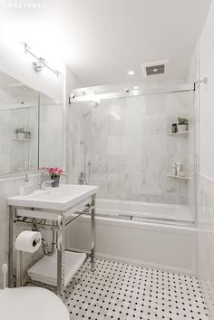 a white bathroom with black and white tile flooring on the shower wall, toilet, sink and bathtub