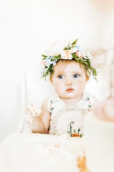 a baby girl with cake on her face and flowers in her hair is looking at the camera