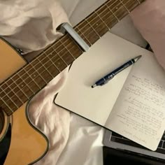 an open notebook with a pen sitting on top of it next to a guitar