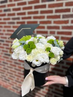 a bouquet of white and green flowers is held in front of a brick wall with a graduate's cap on top