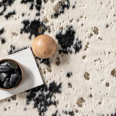 black rocks in a bowl on a white and black patterned rug next to a wooden object