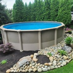 an above ground swimming pool surrounded by rocks and grass with trees in the backround