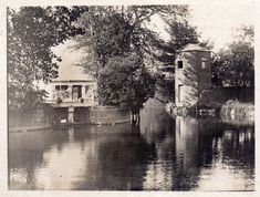 an old black and white photo of a house on the water with trees around it