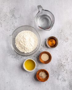 ingredients to make homemade bread laid out in bowls on a gray surface with salt and oil