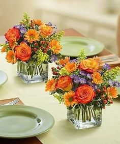 two vases filled with colorful flowers on top of a table next to plates and utensils