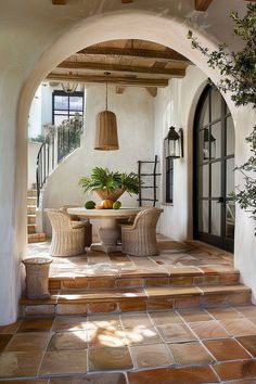 an archway leading to a patio with potted plants on the table and two wicker chairs