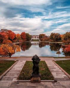 a statue in front of a lake surrounded by trees with orange and red leaves on it