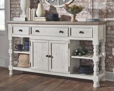 a white wooden buffet table with drawers and plates on the top, in front of a brick wall