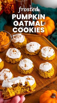 frosted pumpkin oatmeal cookies on a wooden platter with a hand holding one