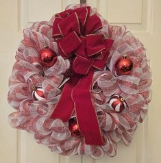 a red and white mesh wreath with ornaments hanging from it's side on a door