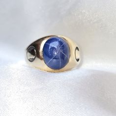 a gold ring with a blue stone in the center on a white fabric background,