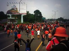 a large group of people are walking down the street in an orange shirt and red hat